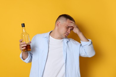 Photo of Man with bottle of whiskey suffering from hangover on orange background