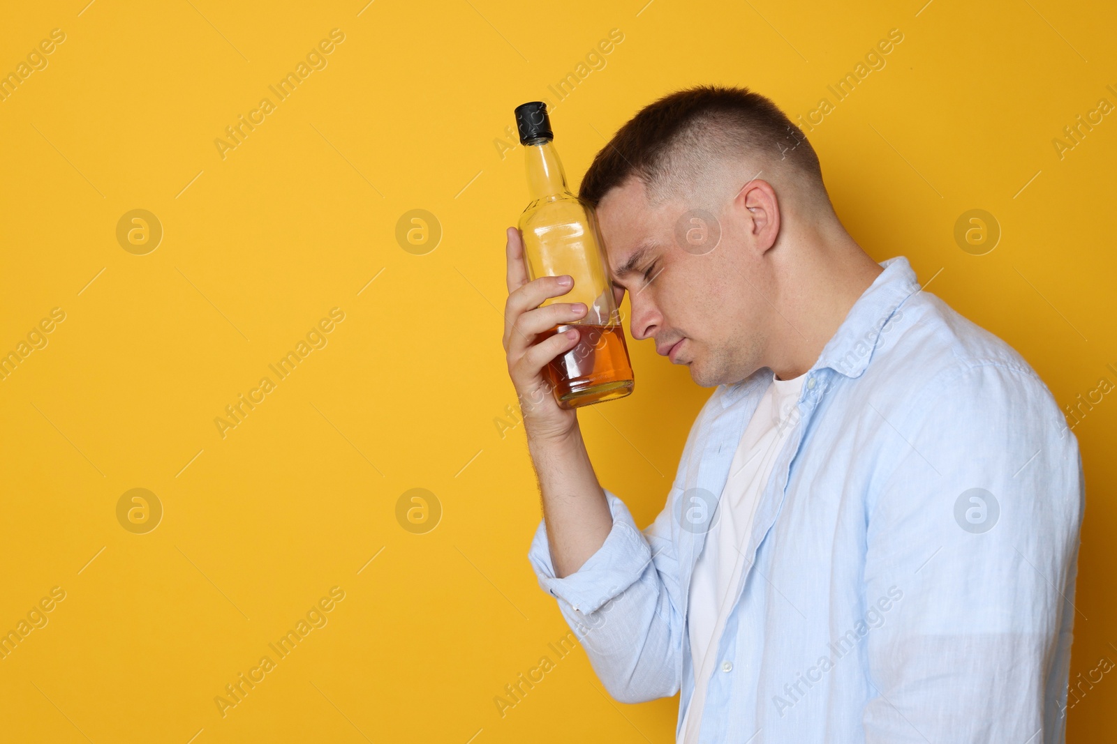 Photo of Man with bottle of whiskey suffering from hangover on orange background, space for text