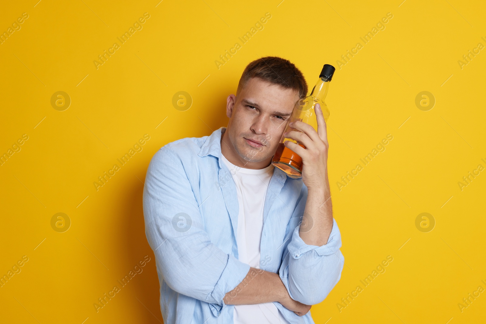 Photo of Man with bottle of whiskey suffering from hangover on orange background