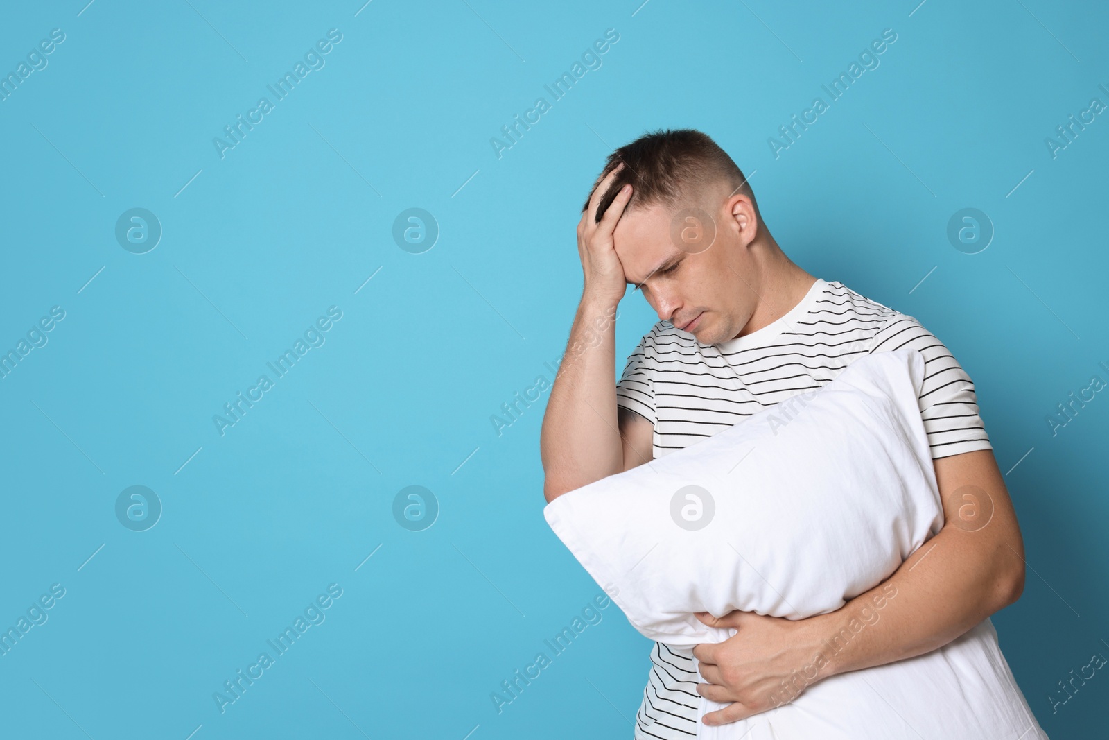 Photo of Man with pillow suffering from hangover on light blue background, space for text