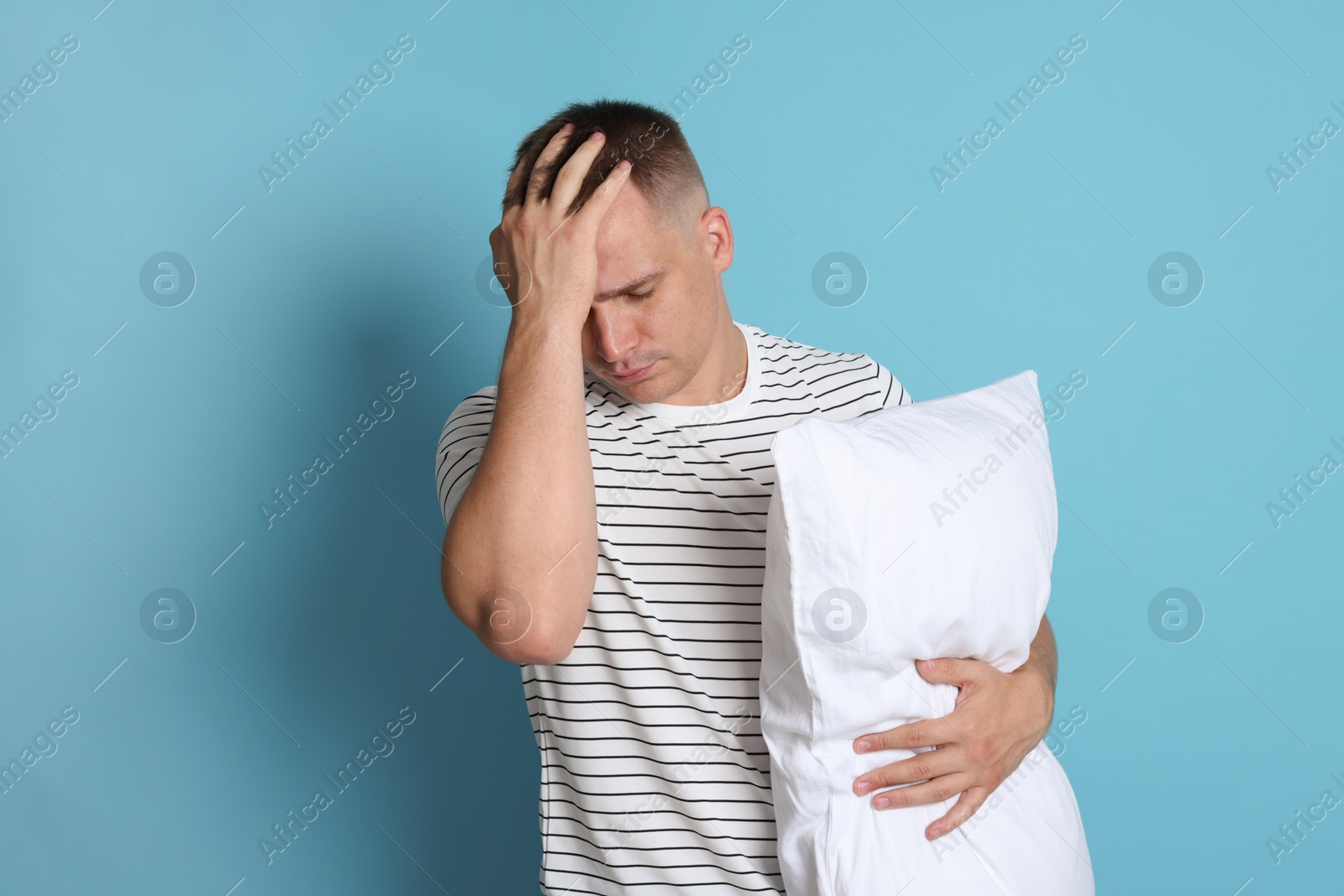 Photo of Man with pillow suffering from hangover on light blue background