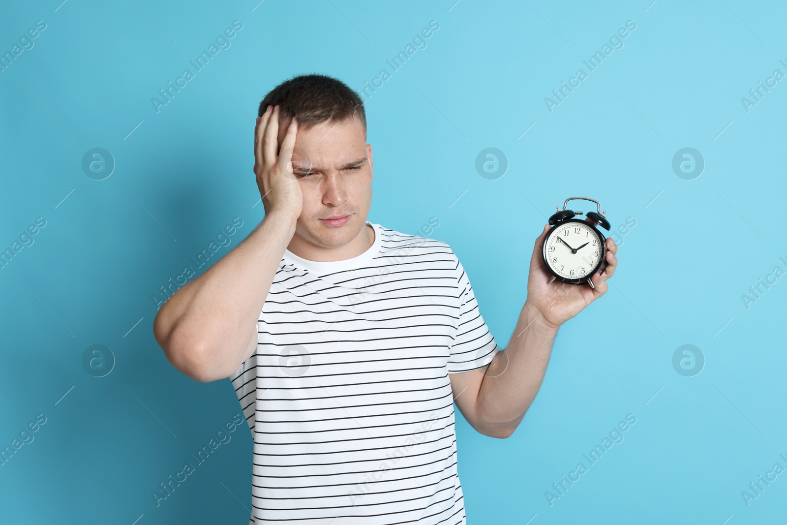 Photo of Man with alarm clock suffering from hangover on light blue background