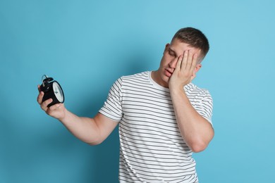 Photo of Man with alarm clock suffering from hangover on light blue background