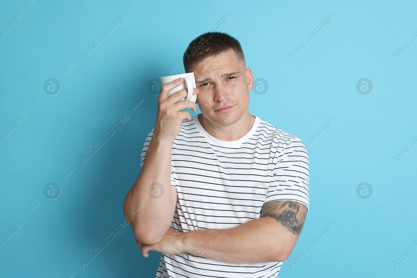 Photo of Man with cup of drink suffering from hangover on light blue background
