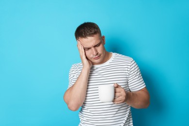 Photo of Man with cup of drink suffering from hangover on light blue background