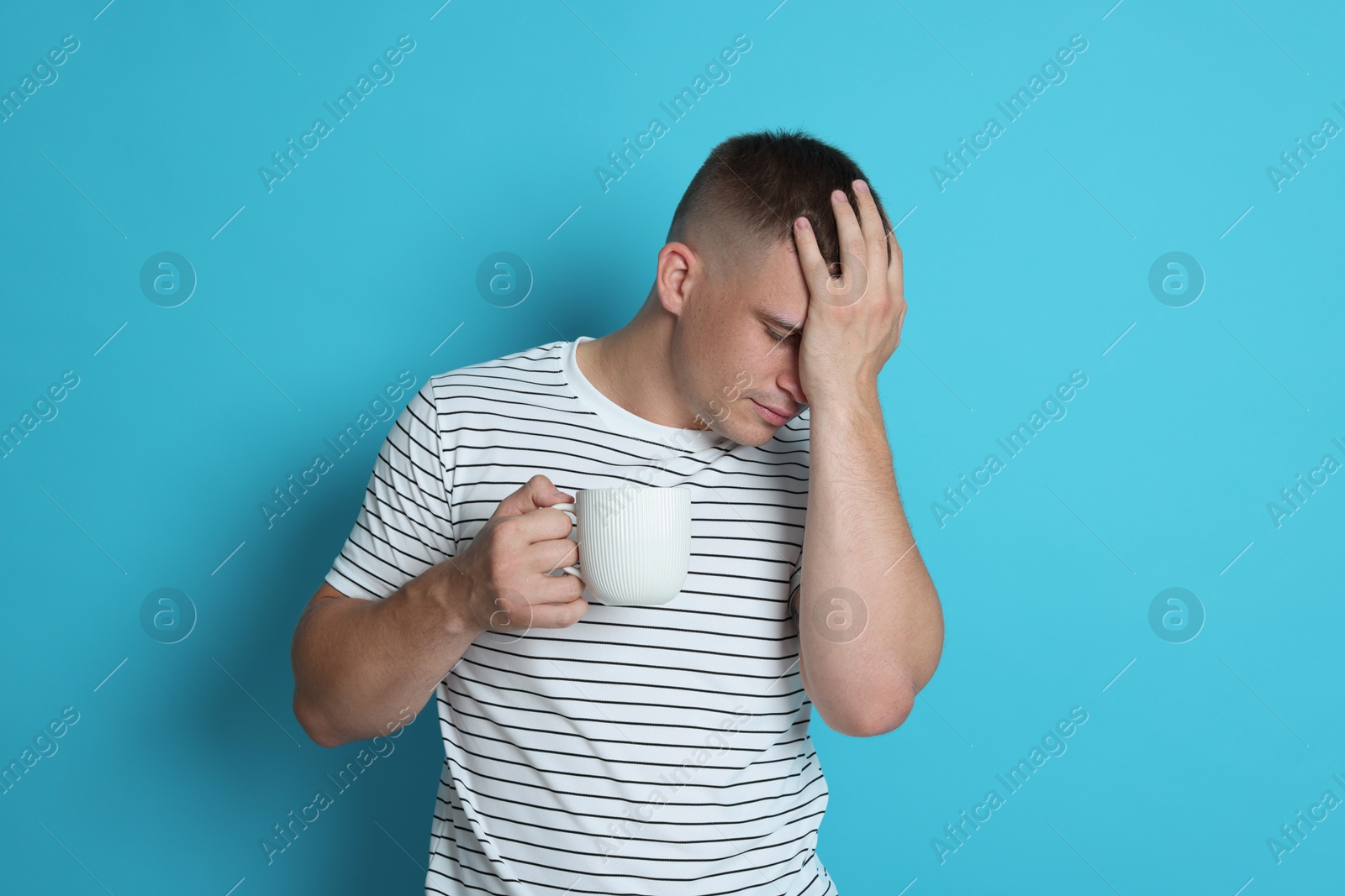 Photo of Man with cup of drink suffering from hangover on light blue background