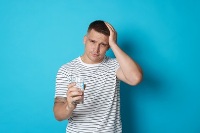 Photo of Man with glass of water suffering from hangover on light blue background