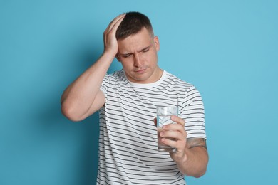 Photo of Man with glass of water suffering from hangover on light blue background