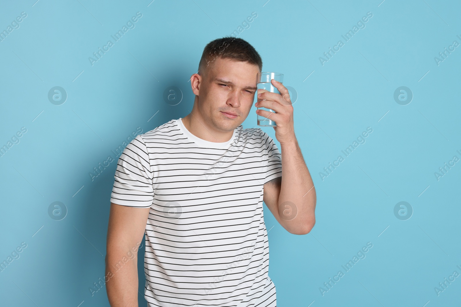Photo of Man with glass of water suffering from hangover on light blue background