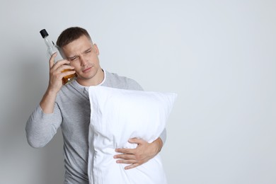 Photo of Man with pillow and bottle of whiskey suffering from hangover on light grey background, space for text