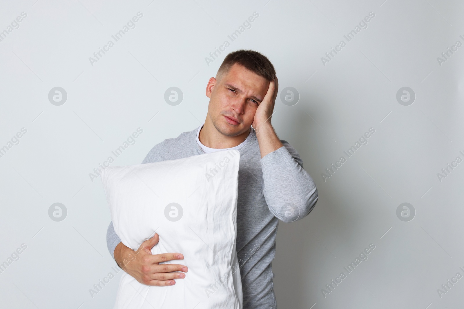 Photo of Man with pillow suffering from hangover on light grey background