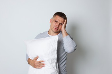 Photo of Man with pillow suffering from hangover on light grey background