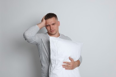 Photo of Man with pillow suffering from hangover on light grey background