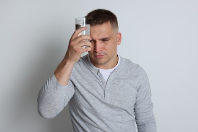 Photo of Man with glass of water suffering from hangover on light grey background