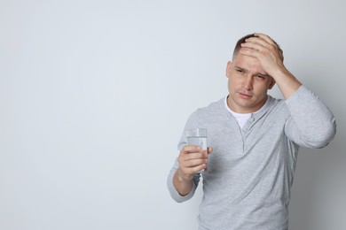 Photo of Man with glass of water suffering from hangover on light grey background, space for text