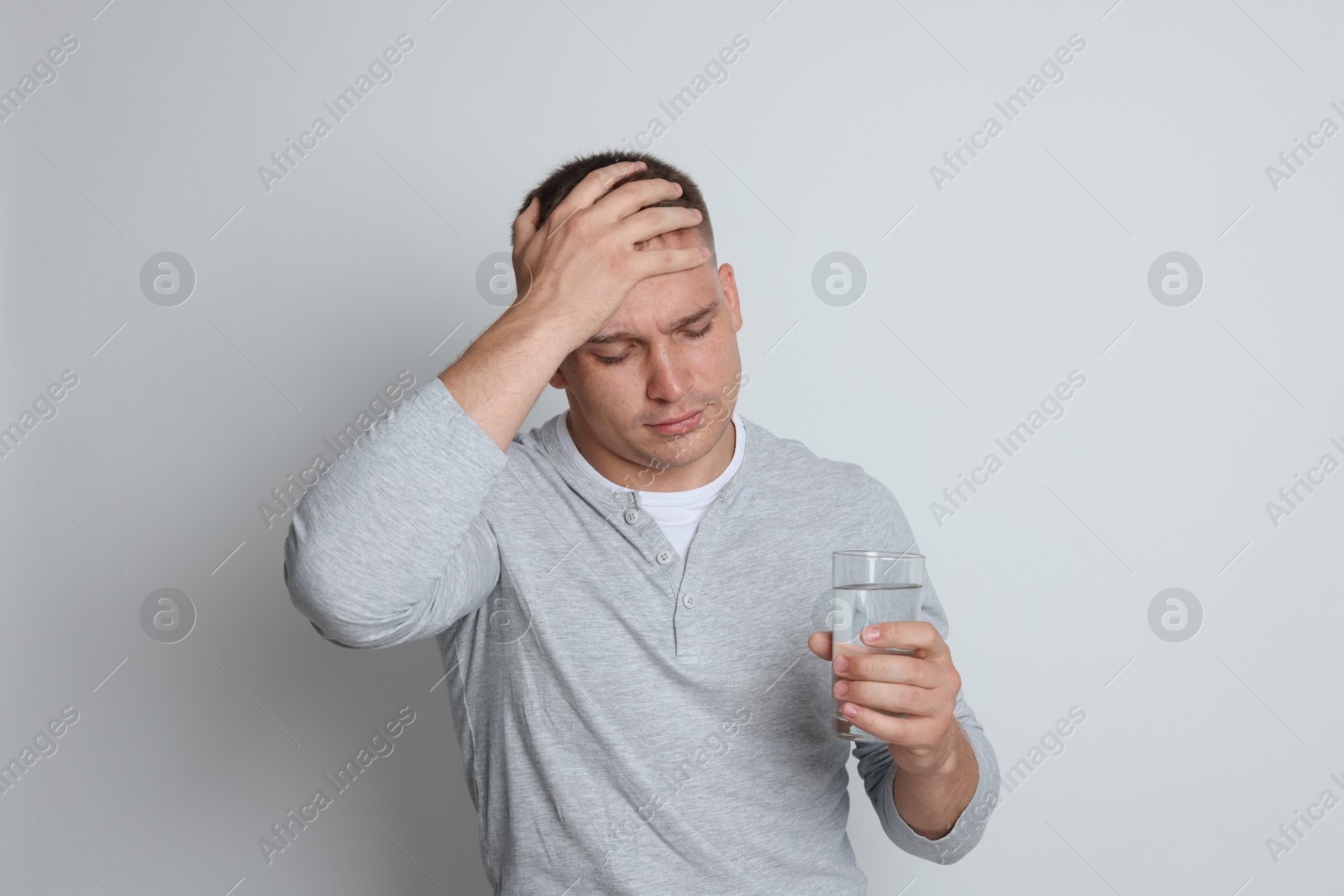 Photo of Man with glass of water suffering from hangover on light grey background