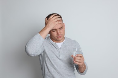 Photo of Man with glass of water suffering from hangover on light grey background