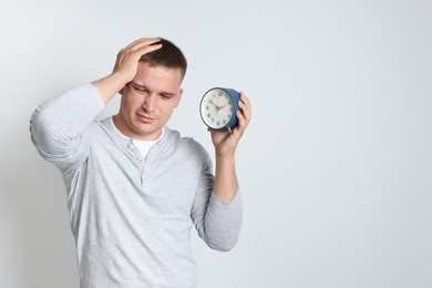 Photo of Man with alarm clock suffering from hangover on light grey background, space for text