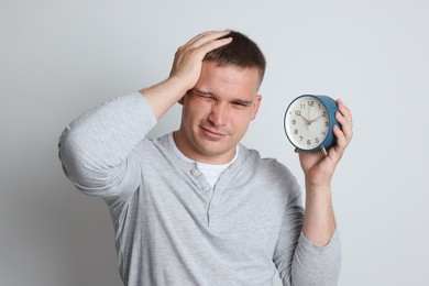 Photo of Man with alarm clock suffering from hangover on light grey background