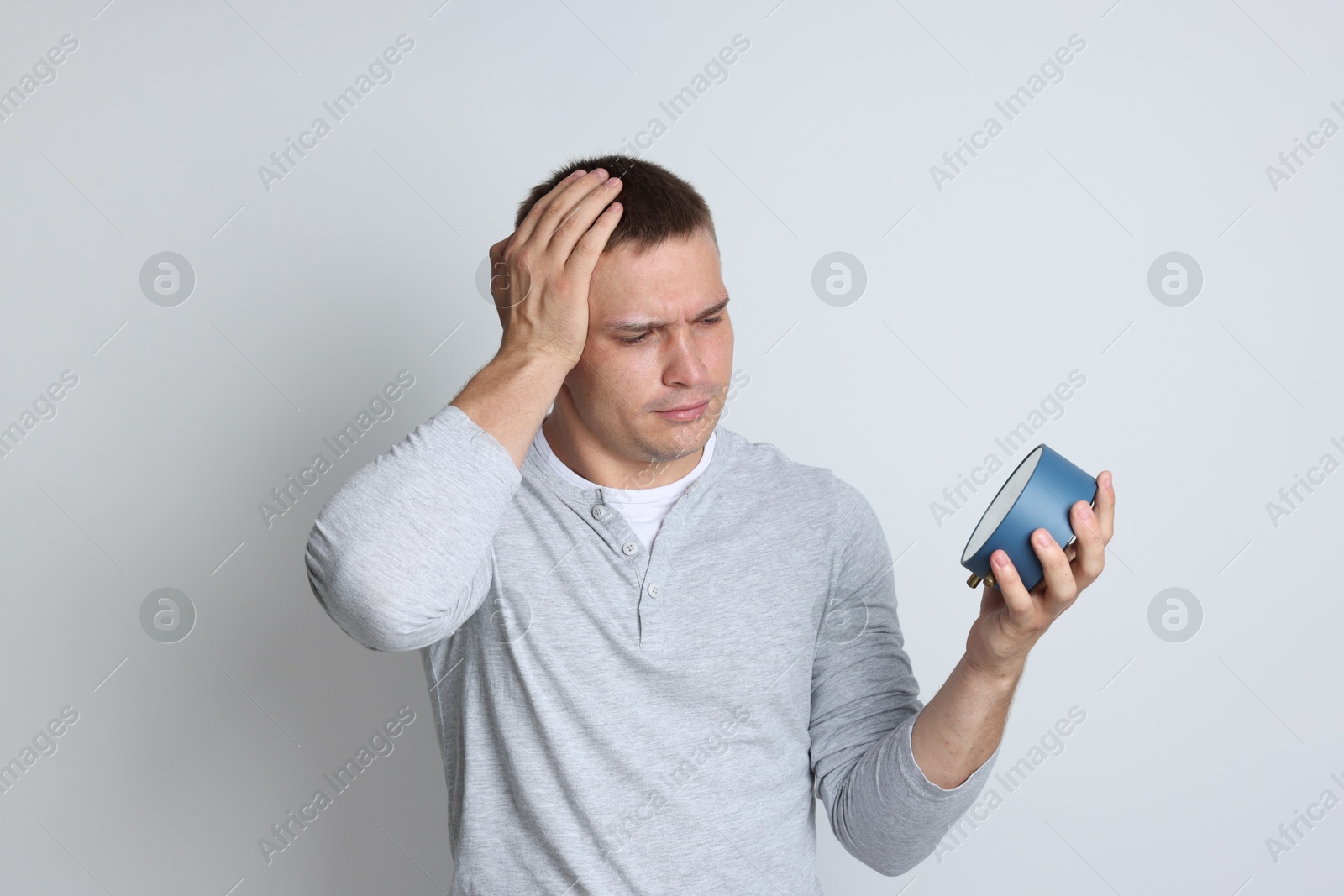 Photo of Man with alarm clock suffering from hangover on light grey background