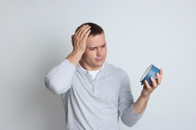 Photo of Man with alarm clock suffering from hangover on light grey background