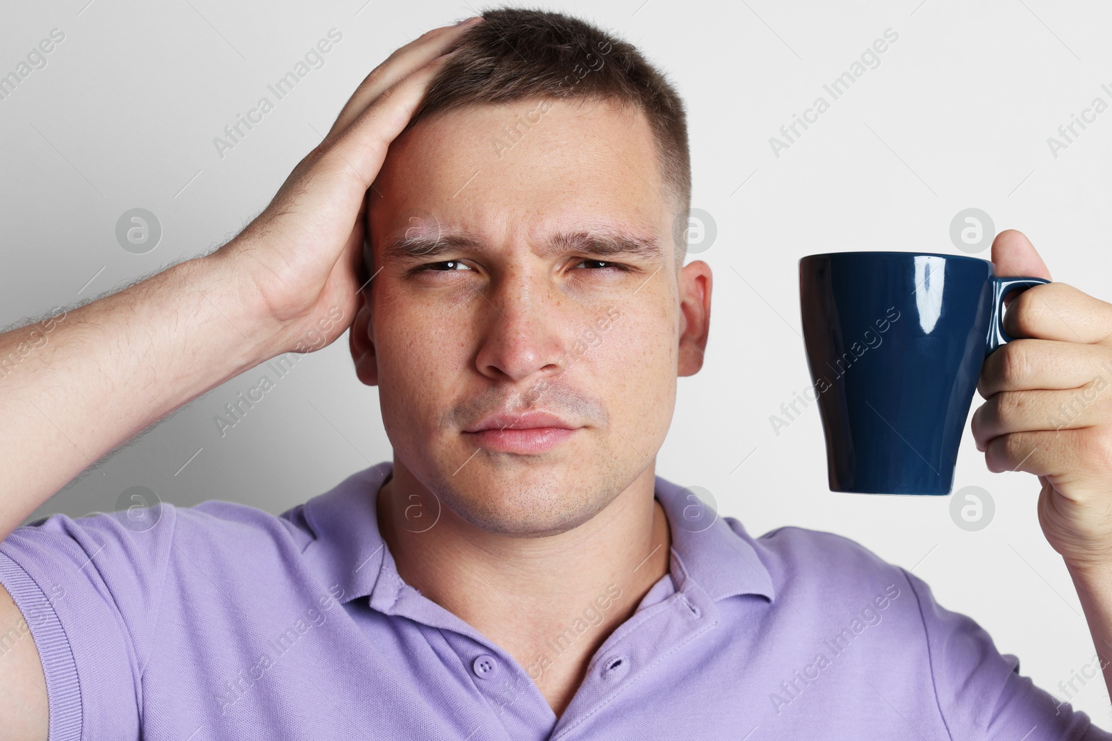 Photo of Man with cup of drink suffering from hangover on light grey background