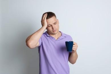 Photo of Man with cup of drink suffering from hangover on light grey background