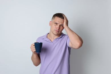 Photo of Man with cup of drink suffering from hangover on light grey background