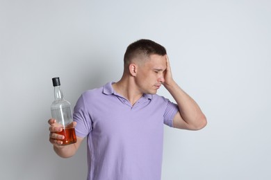 Photo of Man with bottle of whiskey suffering from hangover on light grey background
