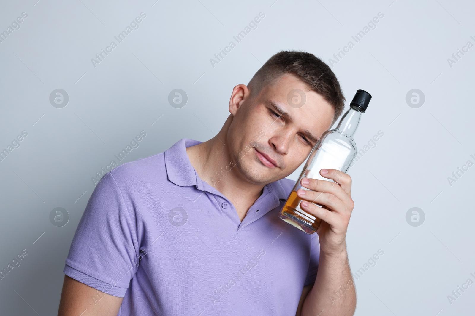 Photo of Man with bottle of whiskey suffering from hangover on light grey background