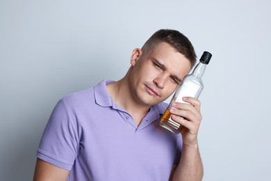 Photo of Man with bottle of whiskey suffering from hangover on light grey background