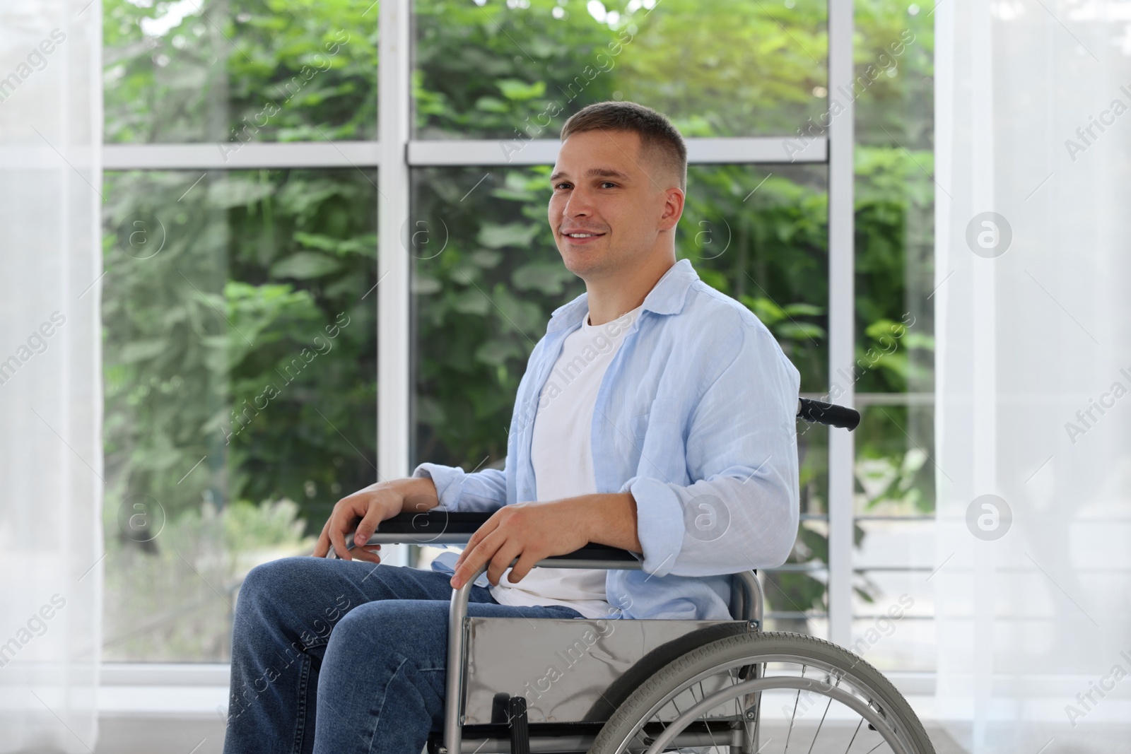 Photo of Young man in wheelchair near window indoors