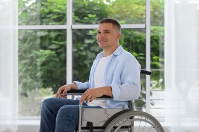 Photo of Young man in wheelchair near window indoors