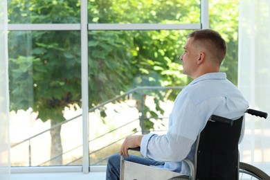Photo of Young man in wheelchair near window indoors