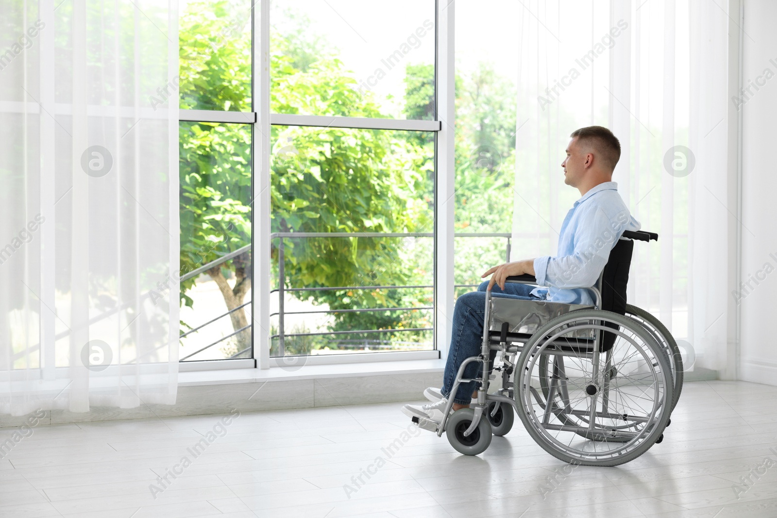 Photo of Young man in wheelchair near window indoors