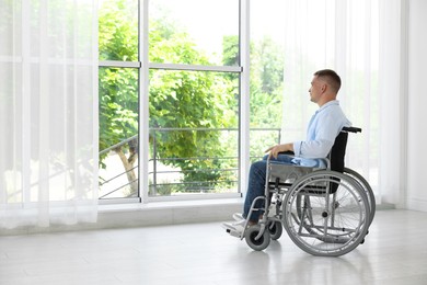 Photo of Young man in wheelchair near window indoors
