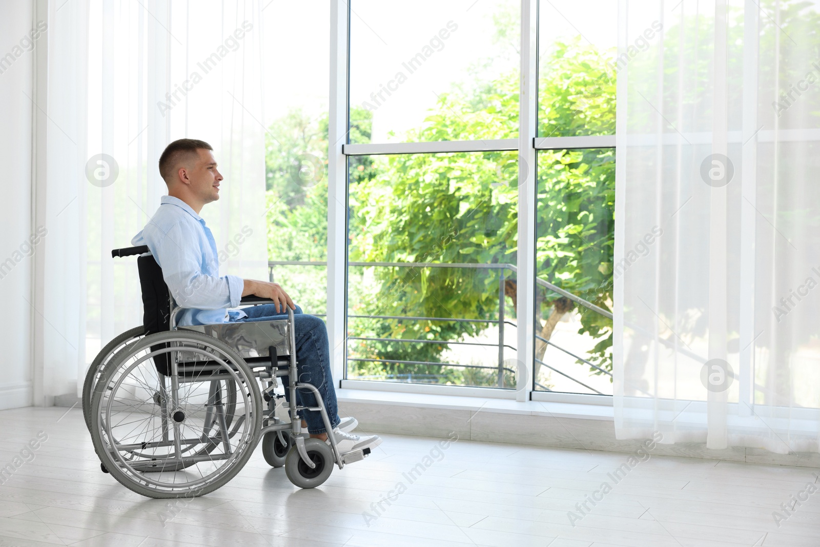 Photo of Young man in wheelchair near window indoors