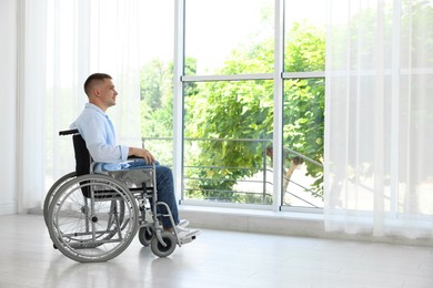 Photo of Young man in wheelchair near window indoors