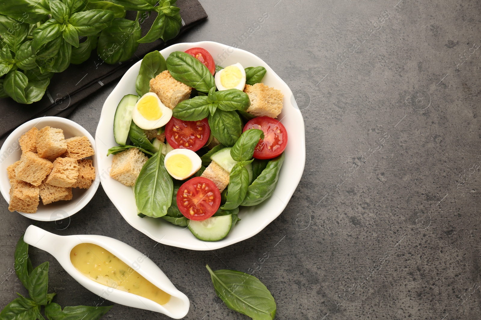 Photo of Tasty salad with croutons, tomatoes, cucumbers and basil on black table, flat lay. Space for text