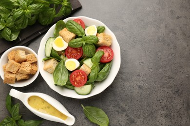 Photo of Tasty salad with croutons, tomatoes, cucumbers and basil on black table, flat lay. Space for text