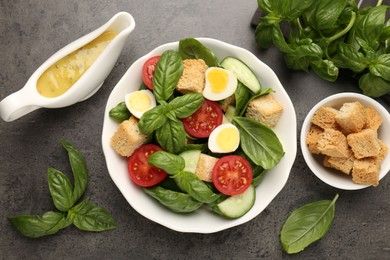 Photo of Tasty salad with croutons, tomatoes, cucumbers and basil on black table, flat lay