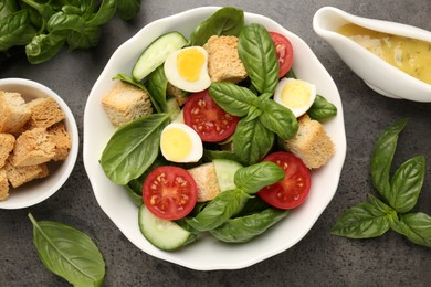 Photo of Tasty salad with croutons, tomatoes, cucumbers and basil on black table, flat lay