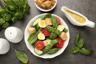 Photo of Tasty salad with croutons, tomatoes, cucumbers and basil on black table, flat lay