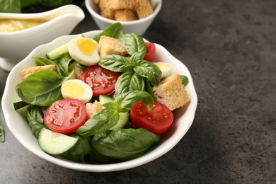 Photo of Tasty salad with croutons, tomatoes, cucumbers and basil on black table, closeup. Space for text