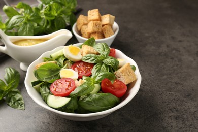 Photo of Tasty salad with croutons, tomatoes, cucumbers and basil on black table, closeup. Space for text