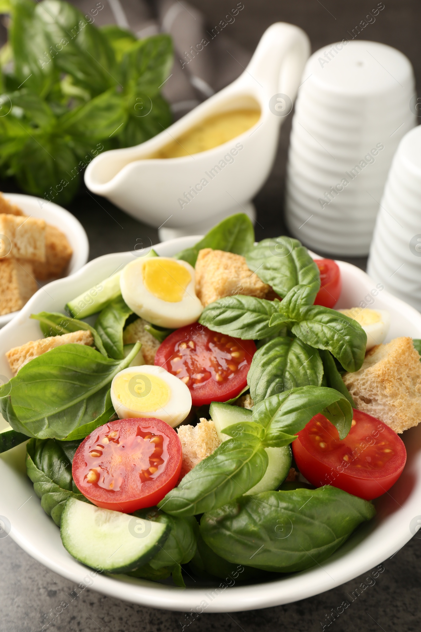 Photo of Tasty salad with croutons, tomatoes, cucumbers and basil on black table, closeup