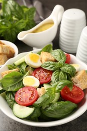 Photo of Tasty salad with croutons, tomatoes, cucumbers and basil on black table, closeup