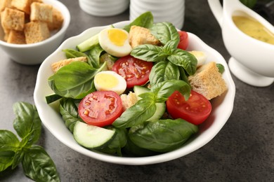 Photo of Tasty salad with croutons, tomatoes, cucumbers and basil on black table, closeup