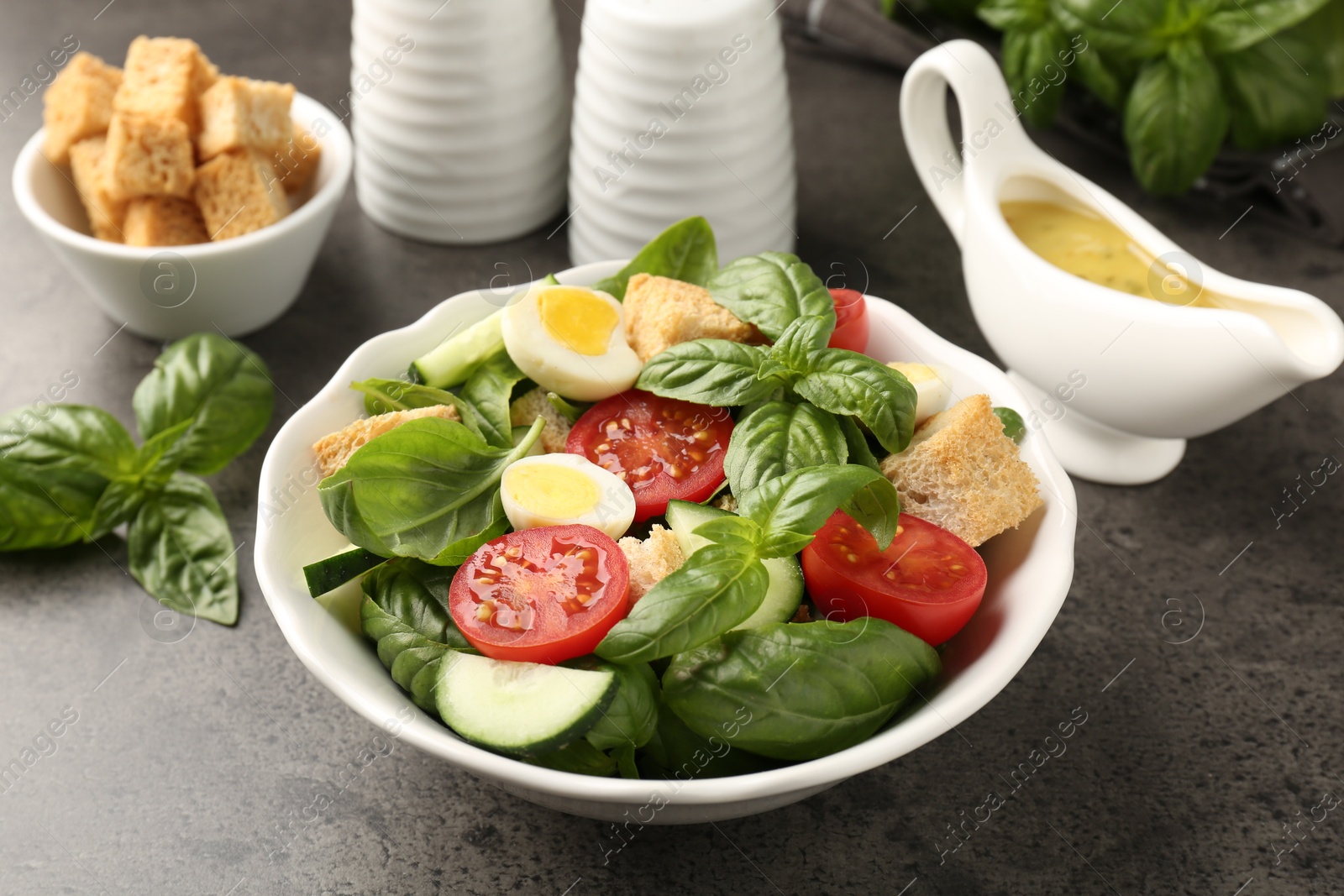 Photo of Tasty salad with croutons, tomatoes, cucumbers and basil on black table, closeup