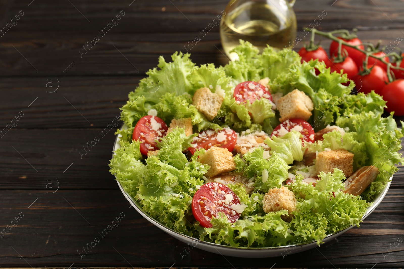 Photo of Tasty salad with croutons, tomatoes, cheese and chicken on black wooden table, closeup. Space for text